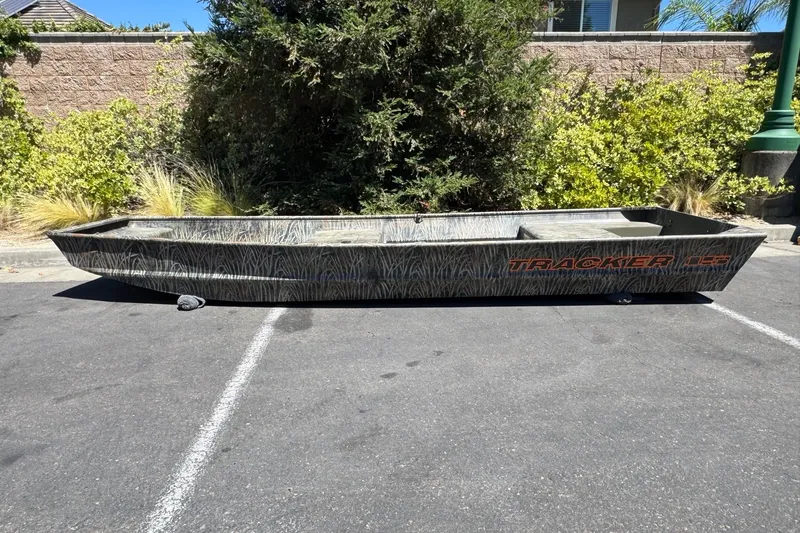 The Image of 2027 Tracker Grizzly 15 Jon boat parked outdoors on asphalt, surrounded by greenery. - 0