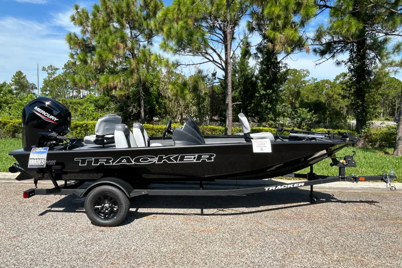 The Image of 2027 Tracker Pro Team 175 boat on trailer, parked outdoors with trees in background. - 0