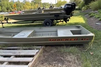 The Image of 2027 Tracker Grizzly 15 Jon boat on grass, with trailer and outboard motor nearby. - 0