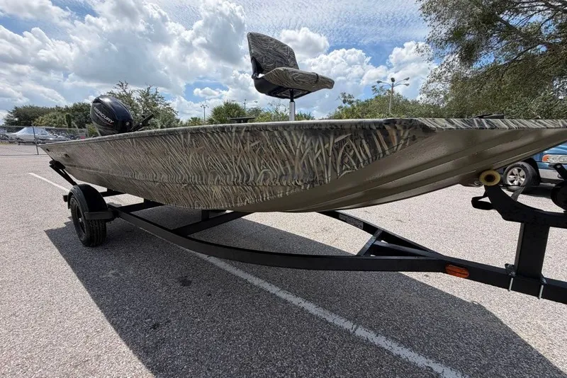 The Image of 2027 Tracker Grizzly 1654 T Sportsman boat on trailer, featuring camouflage design under a cloudy sky. - 0