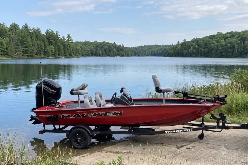 Slide: The Image of 2027 Tracker Pro Team 175 boat on trailer by scenic lake with forest backdrop. - 18