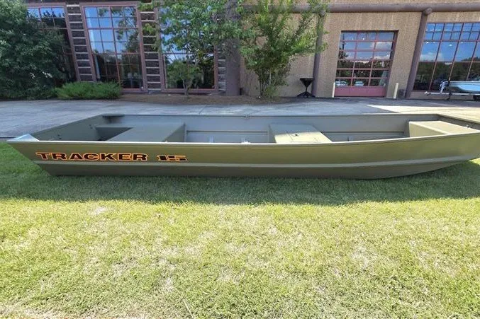 The Image of 2027 Tracker Grizzly 15 Jon boat on grass, near a building with large windows. - 0