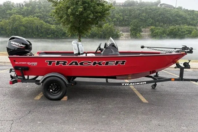 The Image of Red 2027 Tracker Super Guide V-16 SC boat on trailer, parked near a scenic river. - 0