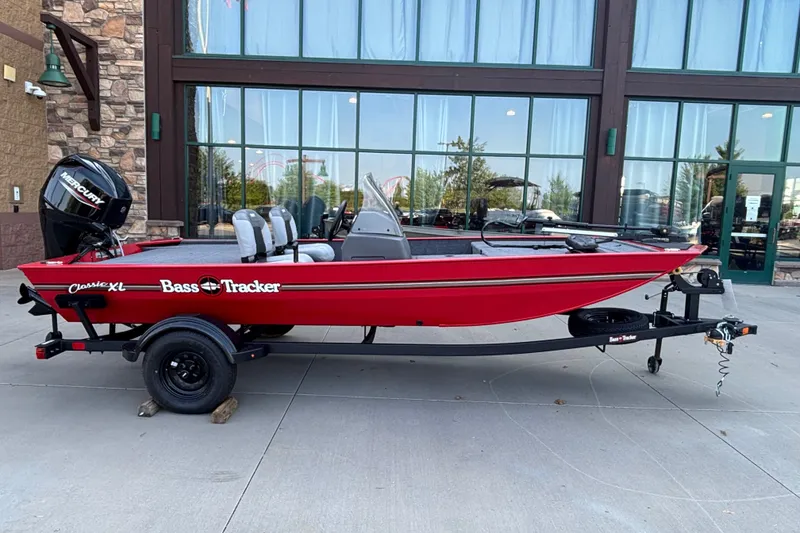 The Image of 2027 Tracker Bass Tracker Classic XL boat in red, parked on a trailer outside a building. - 0