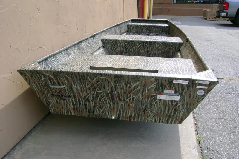 Slide: The Image of 2027 Tracker Grizzly 15 Jon boat with camouflage design, parked outdoors. - 23