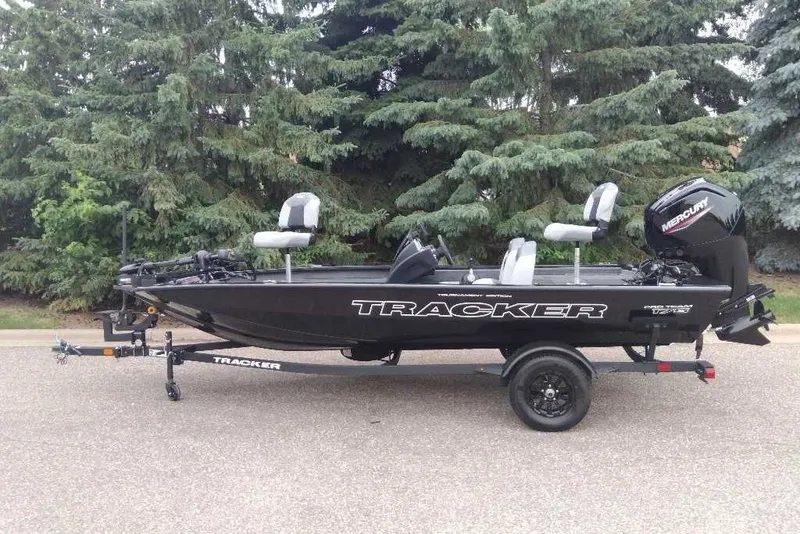 The Image of 2027 Tracker Pro Team 175 boat on trailer, parked near lush green trees. - 0
