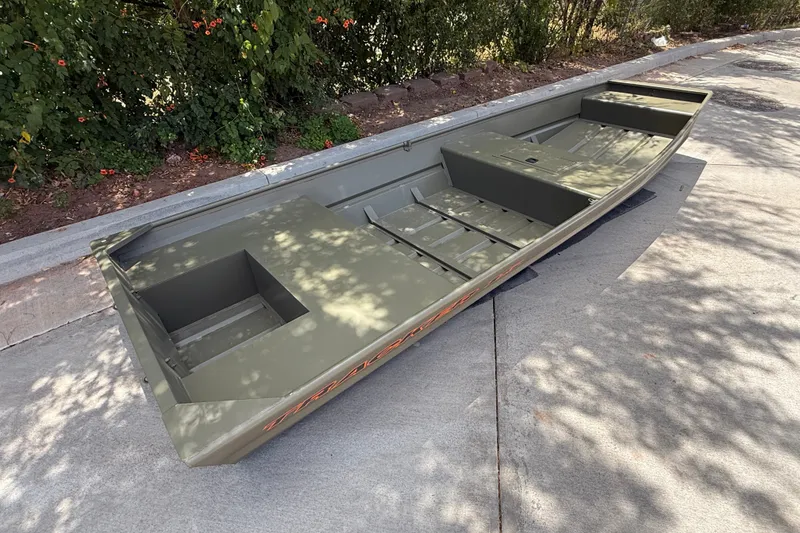 Slide: The Image of 2027 Tracker Grizzly 15 Jon boat on pavement, surrounded by greenery. - 13