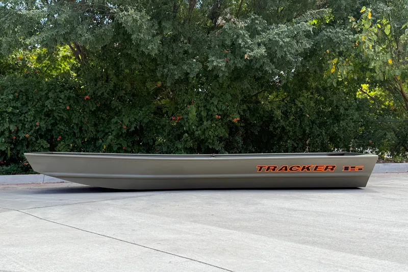 The Image of 2027 Tracker Grizzly 15 Jon boat on pavement, surrounded by lush greenery. - 0