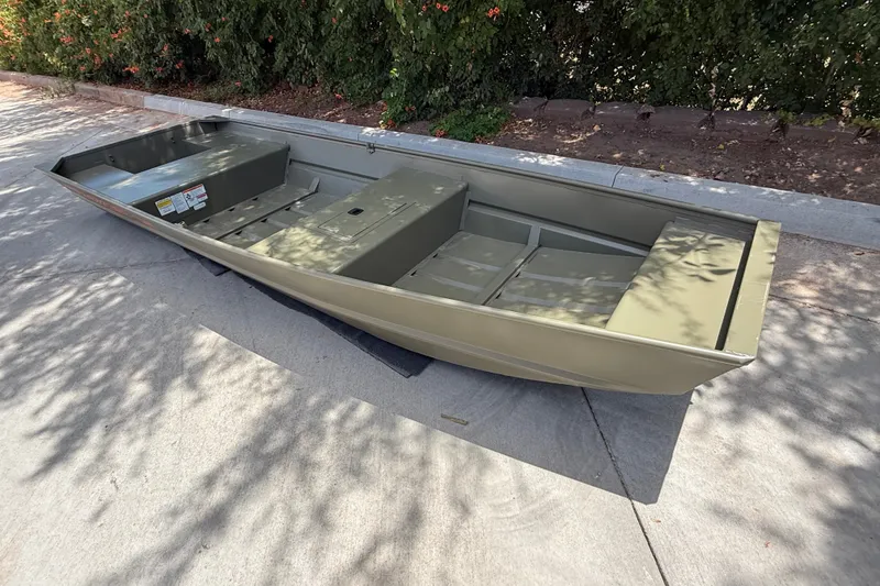 Slide: The Image of 2027 Tracker Grizzly 15 Jon boat on pavement, surrounded by greenery. - 14