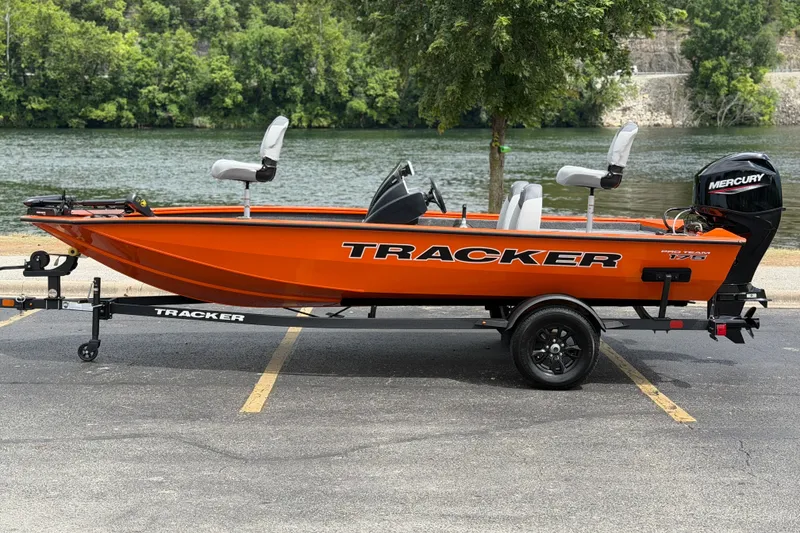The Image of 2027 Tracker Pro Team 175 boat in vibrant orange, parked by a scenic river. - 0