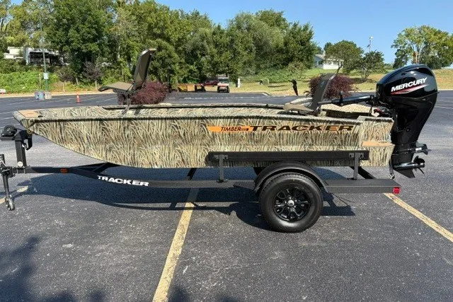 The Image of 2027 Tracker Grizzly 1553 Timber boat with camouflage design on a trailer in a parking lot. - 0