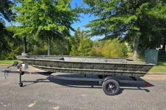 The Image of 2027 Tracker Grizzly 1648 Utility boat on trailer, parked outdoors with trees in background. - 0