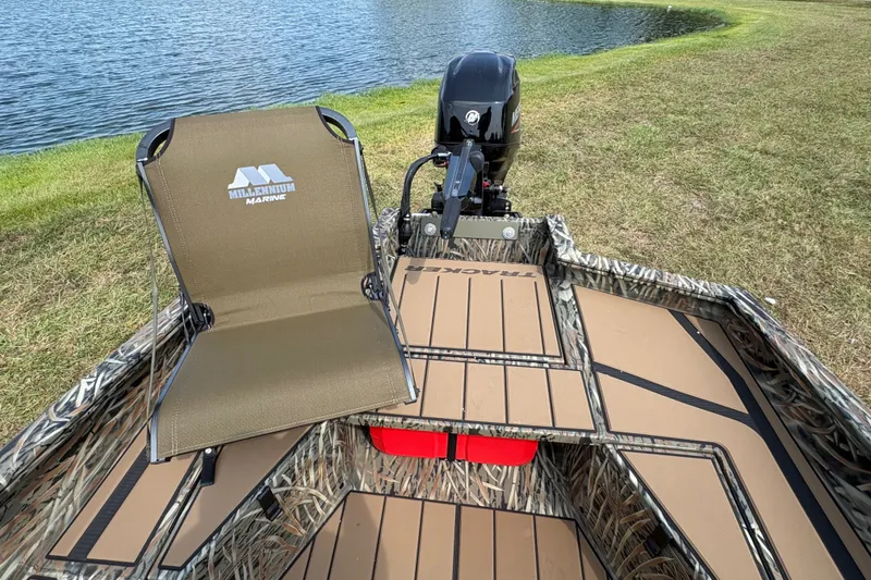 Slide: The Image of 2027 Tracker Grizzly 1553 Timber boat with camo design and Millennium Marine seat by a lake. - 13