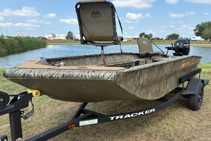 The Image of 2027 Tracker Grizzly 1553 Timber boat on trailer by a lake, featuring camo design. - 0