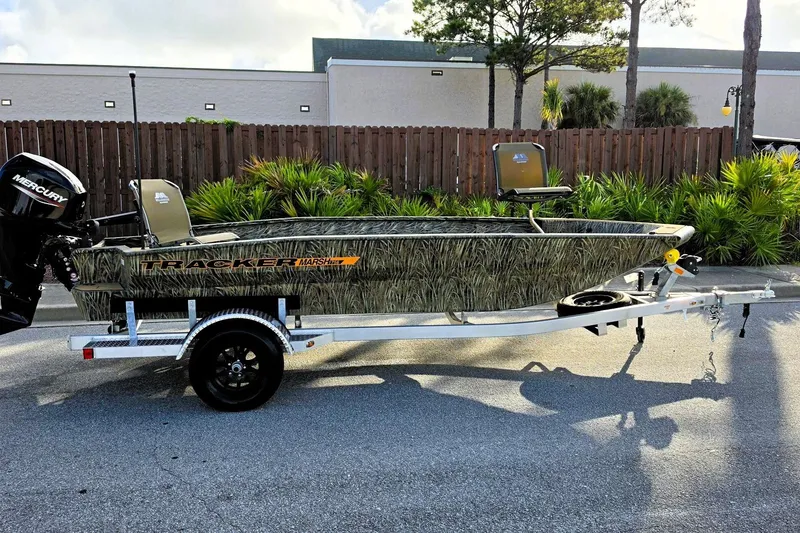The Image of 2027 Tracker Grizzly 1756 T Marsh boat on trailer, camo design, parked outdoors. - 0