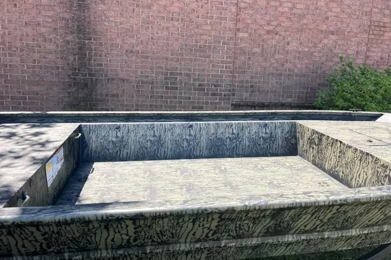 Slide: The Image of 2027 Tracker Grizzly 1648 Utility boat with camouflage pattern, parked near a brick wall. - 14