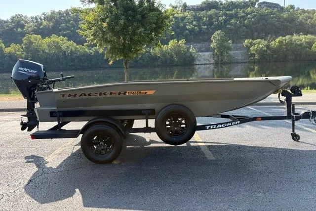 Slide: The Image of 2027 Tracker Grizzly 1553 Timber boat on trailer, parked near a scenic river. - 21
