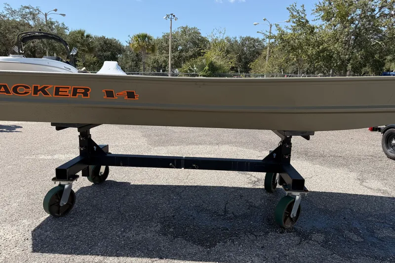The Image of 2027 Tracker Grizzly 14 Jon boat on wheeled stand, outdoors with trees in background. - 0