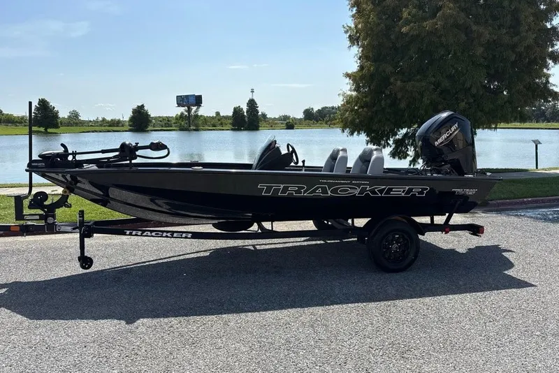 The Image of 2027 Tracker Pro Team 175 boat on trailer by a lake, sunny day. - 0
