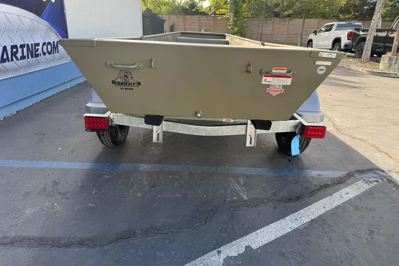 Slide: The Image of 2027 Tracker Grizzly 15 Jon boat on trailer, parked outdoors, rear view. - 19