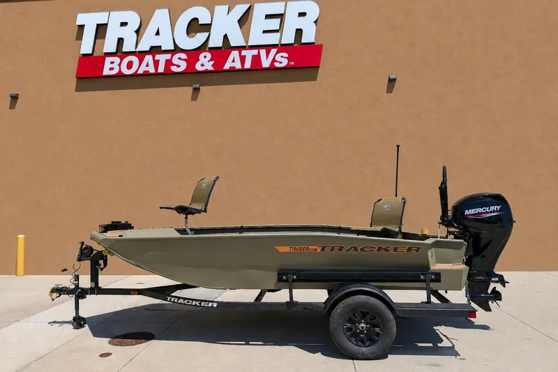 The Image of 2027 Tracker Grizzly 1553 Timber boat on trailer, displayed outside Tracker Boats & ATVs store. - 0