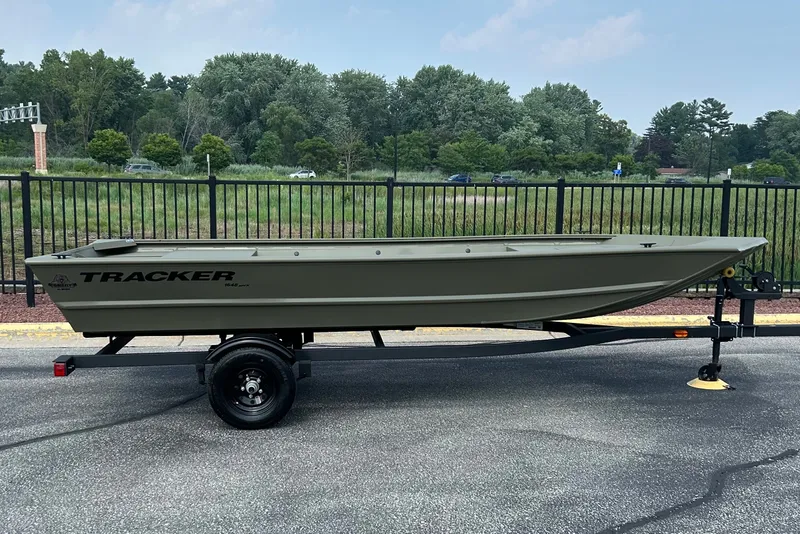The Image of 2027 Tracker Grizzly 1648 Utility boat on trailer, parked outdoors near a fence. - 0