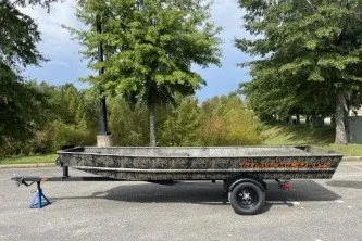 The Image of 2027 Tracker Grizzly 15 Jon boat on trailer, parked outdoors with trees in background. - 0