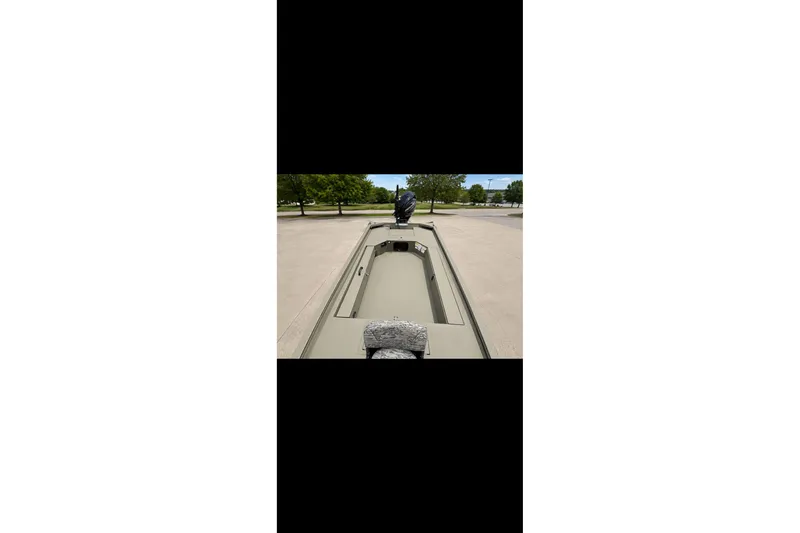 Slide: The Image of 2027 Tracker Grizzly 1654 T Sportsman boat on pavement, surrounded by trees. - 14