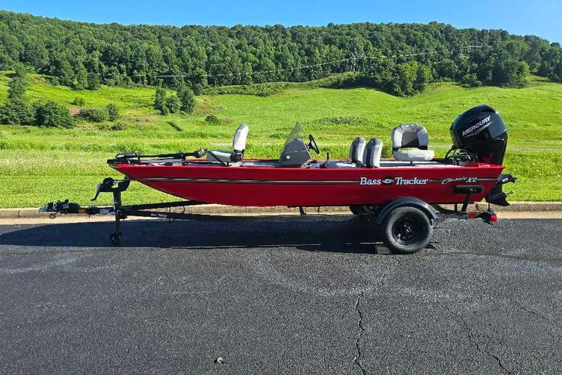 The Image of 2027 Tracker Bass Tracker Classic XL boat on trailer, parked on asphalt with green hills in background. - 0