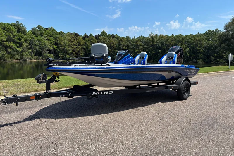The Image of 2027 Nitro Z18 XL boat on trailer, parked by a scenic lake with lush trees. - 0