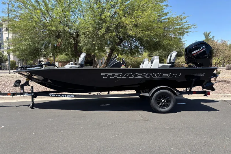 The Image of 2027 Tracker Pro Team 175 boat on trailer, parked outdoors under trees. - 0
