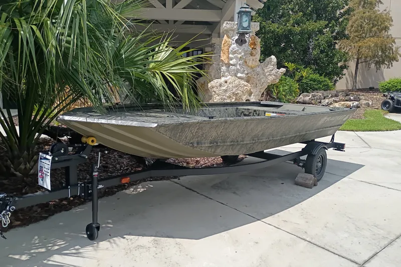 The Image of 2027 Tracker Grizzly 1648 Utility boat on trailer, parked near tropical plants. - 0