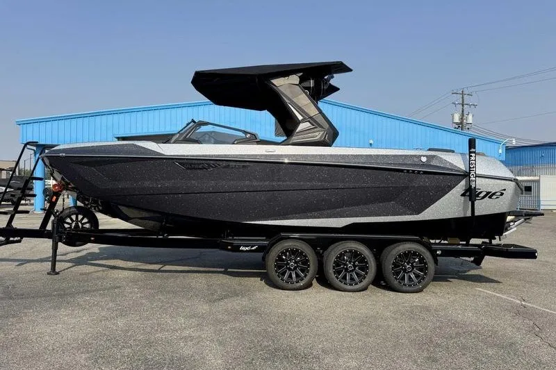 The Image of 2027 Tigé 25ZX boat on trailer, sleek design, parked near blue building. - 0