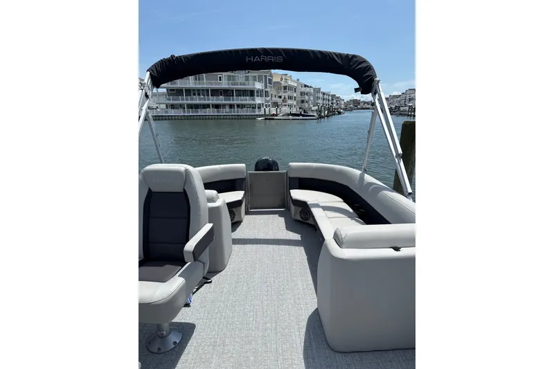 Slide: The Image of 2025 Harris Cruiser 230 pontoon boat with spacious seating, docked by waterfront homes. - 2
