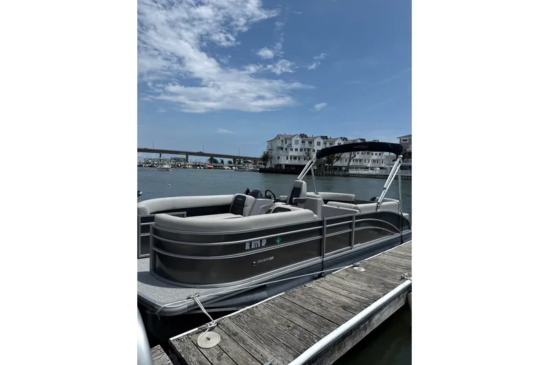 The Image of 2025 Harris Cruiser 230 pontoon boat docked by waterfront buildings under a clear sky. - 1