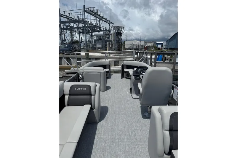 Slide: The Image of 2025 Harris Cruiser 230 pontoon boat with modern seating and steering, docked near industrial area. - 5
