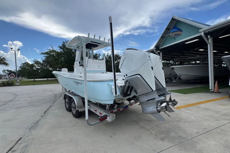 Slide: The Image of 2027 Caymas 281 HB boat on trailer, dual engines, parked near a marina under cloudy sky. - 18