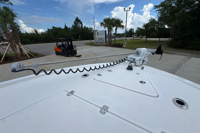 Slide: The Image of 2027 Caymas 281 HB boat deck with trolling motor, parked near a forklift and palm trees. - 23