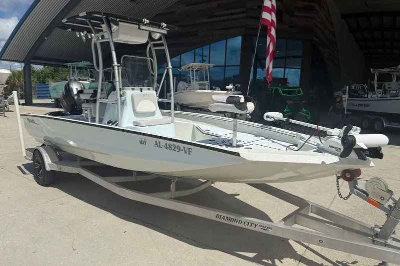 Slide: The Image of 2021 Excel 203 Bay Pro boat on trailer, parked outdoors with American flag. - 2