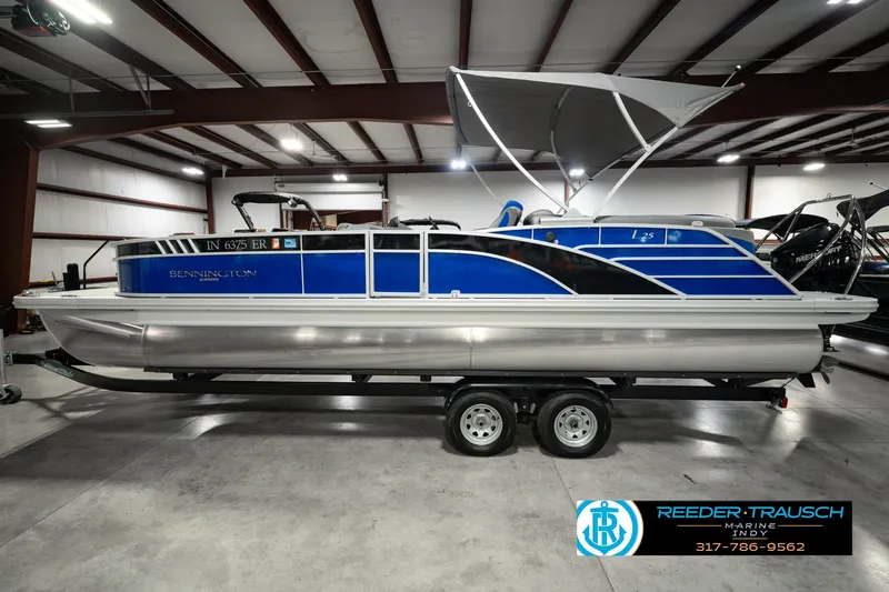 Slide: The Image of 2025 Bennington L 25 Quad Bench Bowrider pontoon boat in showroom, blue and silver design. - 12