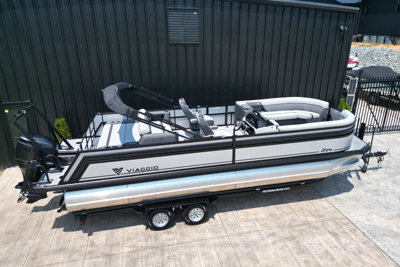 Slide: The Image of 2027 Viaggio Lago X-S 24 pontoon boat on trailer, parked by black building. - 20