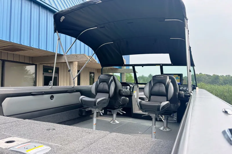 Slide: The Image of 2025 Lund 2275 Baron boat interior with canopy and seating, parked near a blue building. - 13