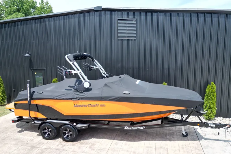 Slide: The Image of 2022 MasterCraft NXT24 boat with cover on trailer, parked by a black building. - 14