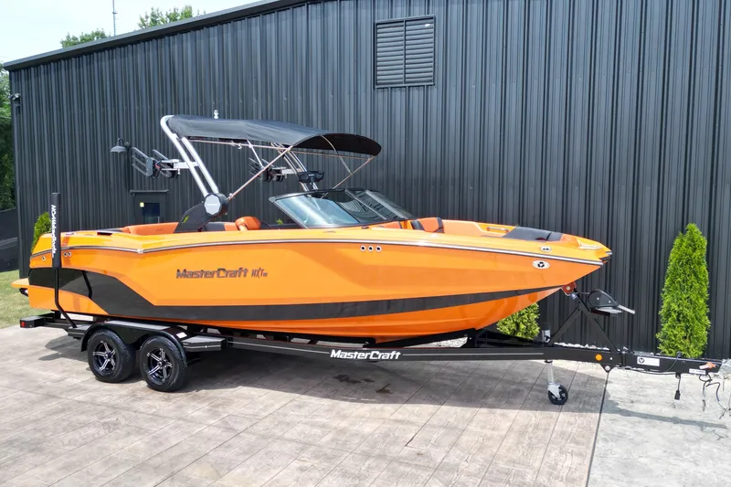 Slide: The Image of 2022 MasterCraft NXT24 boat in vibrant orange on a trailer, parked outdoors. - 23