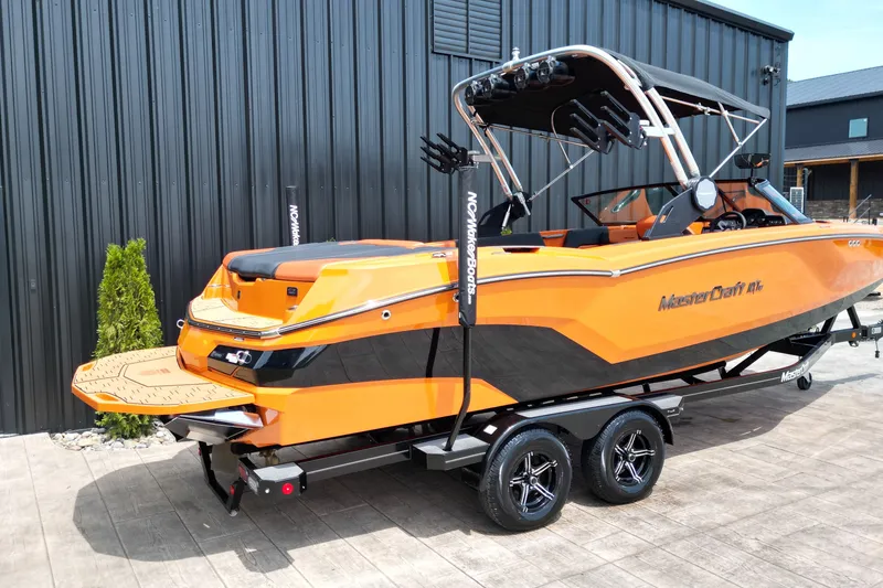 Slide: The Image of 2022 MasterCraft NXT24 boat in vibrant orange on a trailer, parked outdoors. - 21