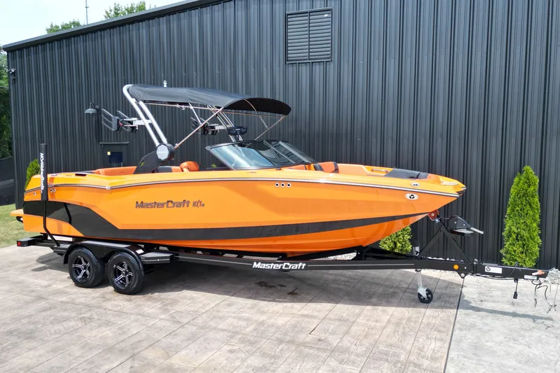 Slide: The Image of 2022 MasterCraft NXT24 boat in vibrant orange on a trailer, parked outdoors. - 22