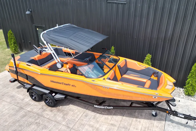 Slide: The Image of 2022 MasterCraft NXT24 boat in vibrant orange, parked on a trailer beside a black building. - 19