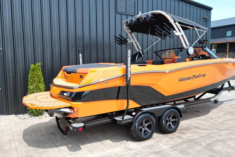Slide: The Image of 2022 MasterCraft NXT24 boat in vibrant orange on a trailer, parked outdoors. - 20