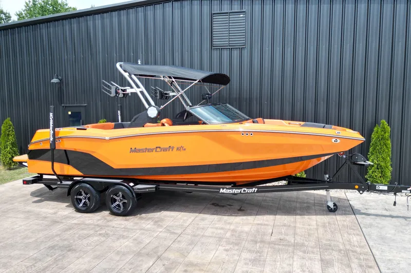 Slide: The Image of 2022 MasterCraft NXT24 boat in vibrant orange on a trailer, parked outdoors. - 1