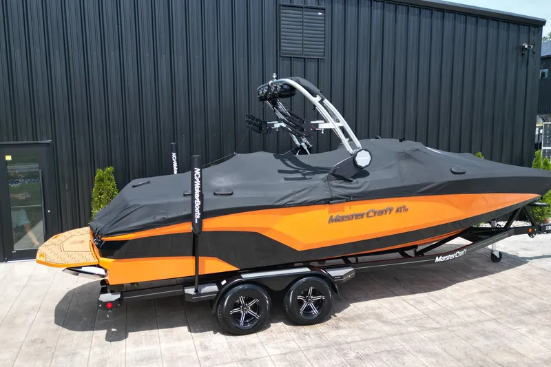 Slide: The Image of 2022 MasterCraft NXT24 boat with orange and black design, covered and on a trailer. - 12